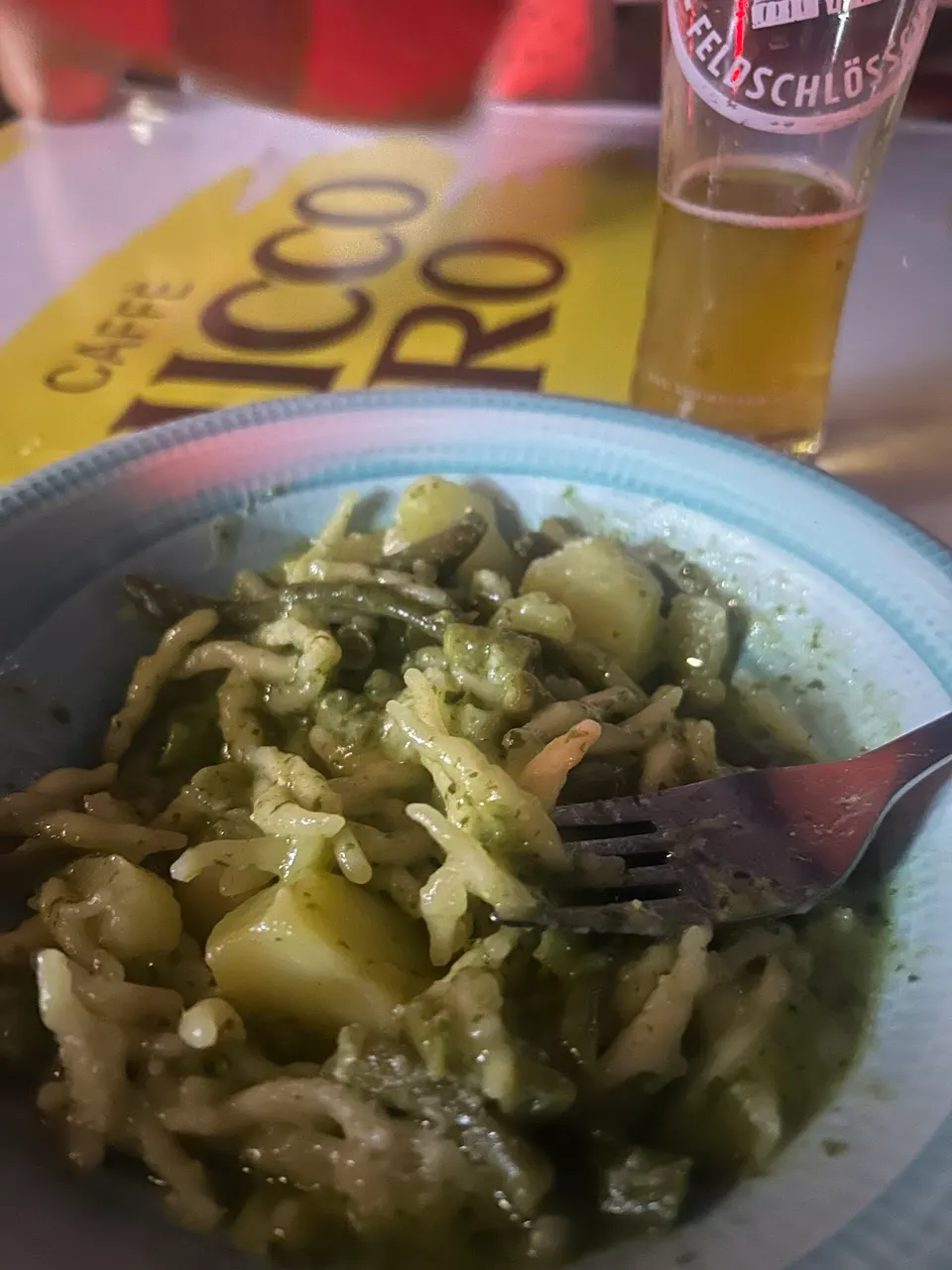 Piatto di pasta al pesto con patate, accanto a un bicchiere di birra