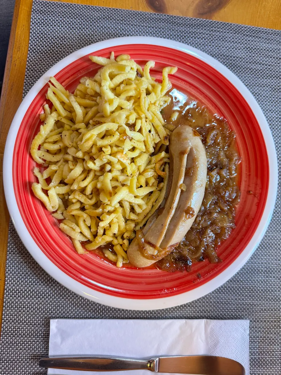 Piatto di spätzli con una salsiccia e salsa scura di cipolle