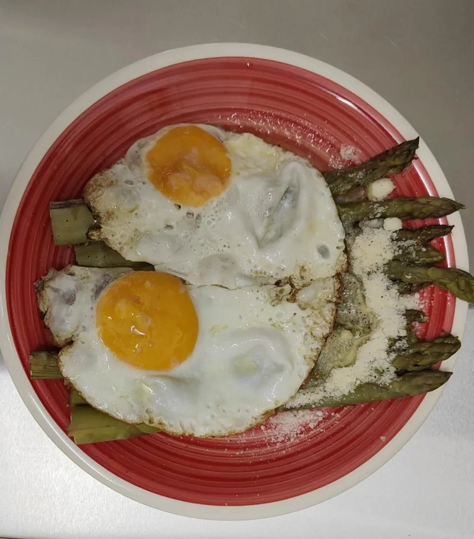 Due uova all’occhio di bue su asparagi verdi con formaggio grattugiato